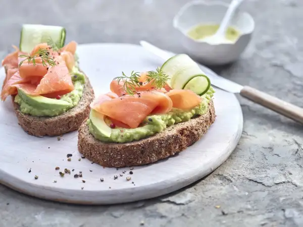 Deux toasts avocat saumon, garniture fraîche avec concombre et aneth, sur pain complet.