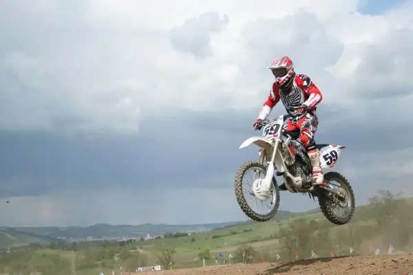 Motocrossowiec w skoku na motocyklu, podobnym do Husqvarna Motorcycles i KTM, w czerwono-białym stroju.