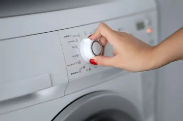 Main d'une femme sélectionnant le programme synthétique sur une machine à laver.