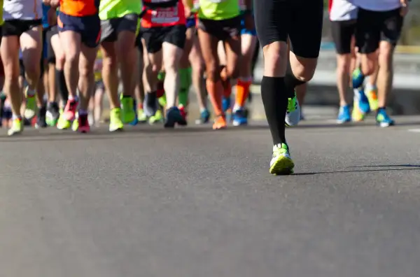 Gambe di corridori in maratona, con scarpe colorate. Un esempio di tabella maratona 4 allenamenti settimanali.