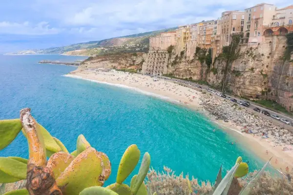 Vue panoramique de la plage de Tropea, Calabre, avec ses eaux turquoise, ses falaises et ses maisons colorées perchées.