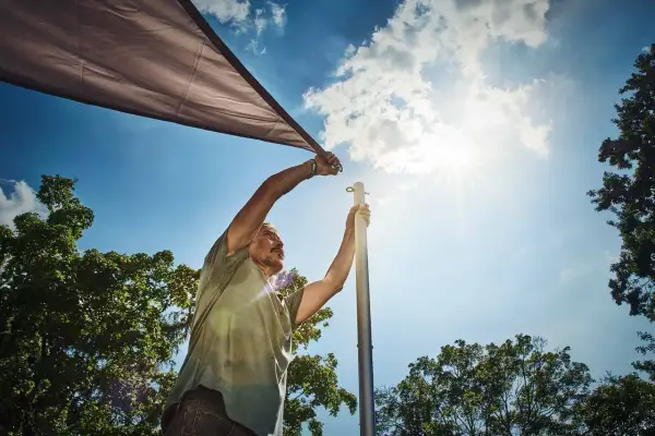 Man sätter upp ett solsegel mot en klarblå himmel med solens strålar som lyser.