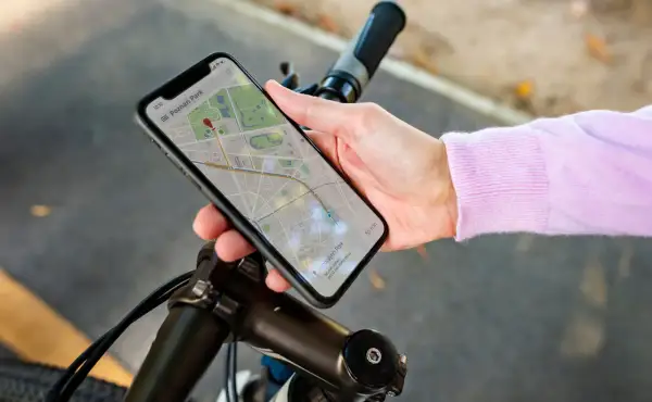 Dłoń trzyma smartfon z mapą, wskazującą trasę rowerową. Telefon pełni rolę licznika na rower, pokazując drogę do celu.