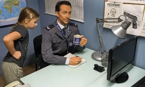 W muzeum Ojca Mateusza dziewczynka przygląda się woskowemu policjantowi z kubkiem "POLICJA".