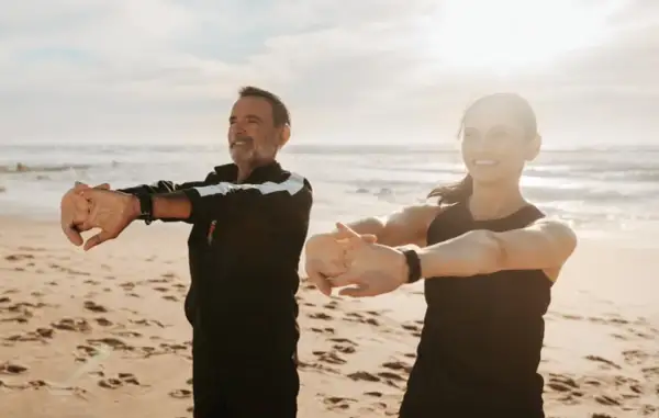 Para ćwiczy na plaży, ciesząc się słońcem i morzem. Idealne miejsce na turnusy rehabilitacyjne nad morzem.