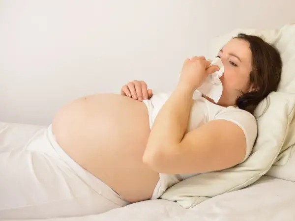 Gravid kvinna med andfåddhet ligger i sängen och snyter sig i en näsduk.