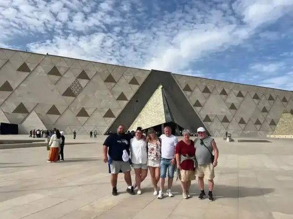Rodzina pozuje przed nowoczesnym, geometrycznym budynkiem – nowym muzeum w Egipcie.