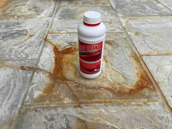 Schody wejściowe z granitu płomieniowanego z plamami rdzy. Butelka środka Rust Cleanze, który pomoże usunąć rdzę.