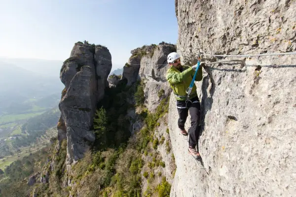 Un homme équipé pour la via ferrata progresse sur une paroi rocheuse, profitant d'un paysage spectaculaire.