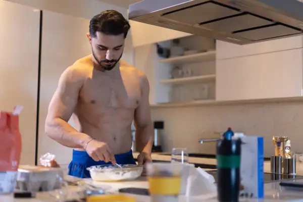 Muskulöser Mann bereitet in der Küche eine Mahlzeit zu. Kohlenhydrate sind wichtig für den Muskelaufbau.
