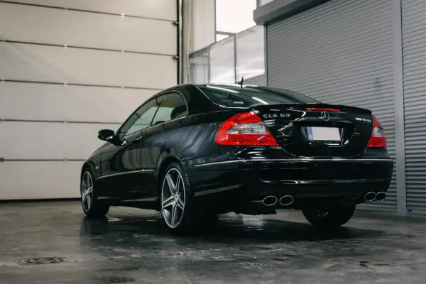 Czarny Mercedes CLK 63 AMG z podwójnymi końcówkami wydechu, zaparkowany w garażu z podnoszoną bramą.