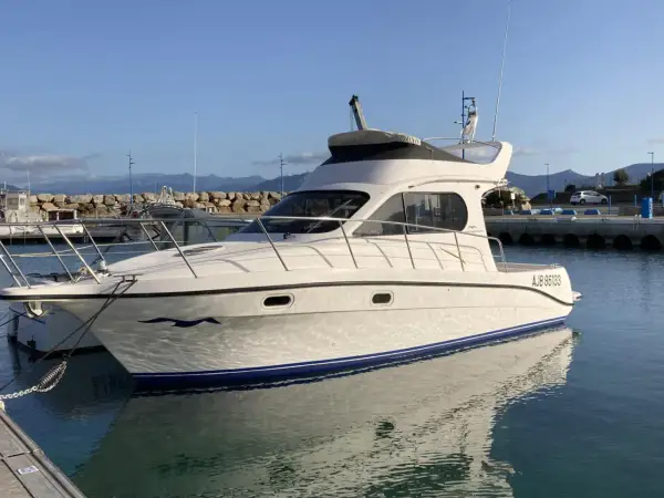 Yacht Intermare 30 ormeggiato in porto, con riflessi sull'acqua calma. Montagne sullo sfondo.