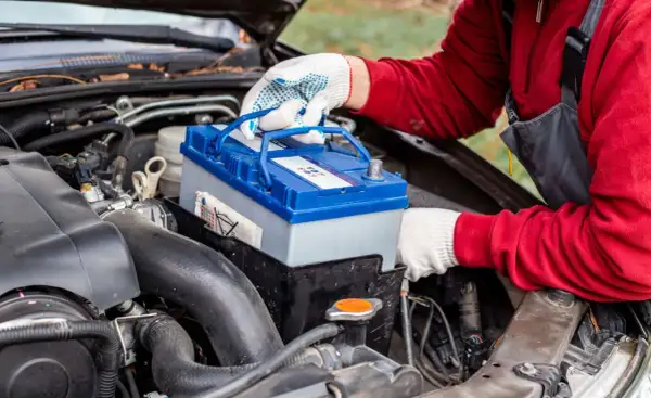 Persona con guantes blancos manipula una batería de coche azul y gris, lista para cargar batería coche.