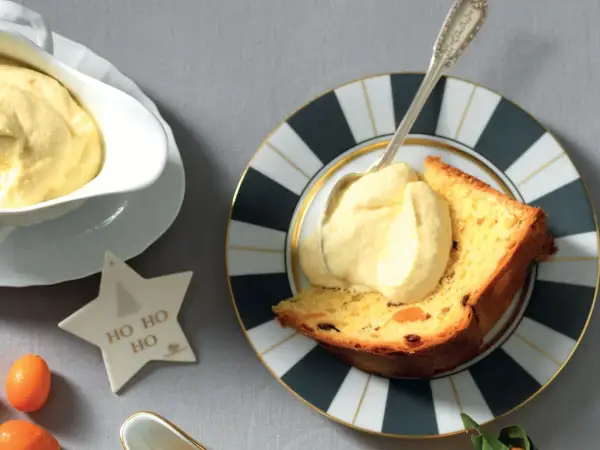 Una fetta di panettone con abbondante crema al mascarpone, servita su un piatto decorato. Un'idea golosa per le feste.