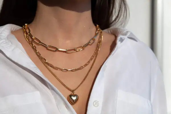 Tres collares dorados en capas, uno con un corazón, lucen perfectos con el escote de una camisa blanca.