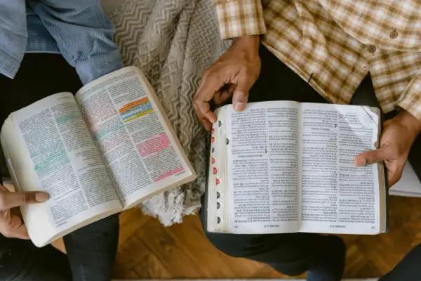 Dwie osoby studiują Biblię, analizując podział ksiąg biblijnych. Widać fragmenty z kolorowymi zakreśleniami.