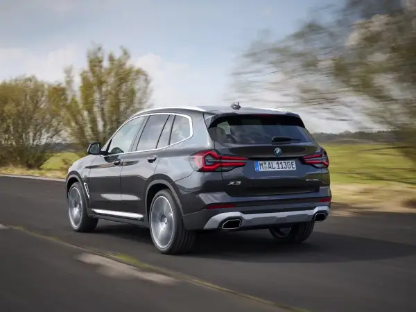 Ciemnoszary BMW X3 xDrive pędzi po drodze, otoczony zielenią i rozmazanymi drzewami.