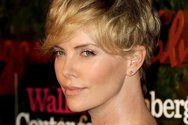Charlize Theron w fryzurze pixie, która dodaje objętości cienkim włosom, z subtelnym makijażem i złotą biżuterią.