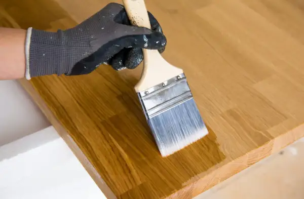 Maintenant, peut on vernir après huile de lin ? Un pinceau applique une couche transparente sur un plateau en bois.