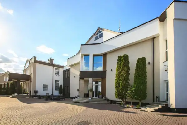 Nowoczesny budynek hotelu Santana Białystok z podjazdem z kostki brukowej i zielenią.
