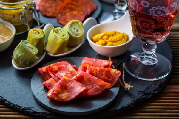 Leckere Tapas Ideen: Chorizo, eingelegte Artischocken und Senf mit einem Glas Rotwein.