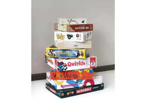 Stos pudeł z grami planszowymi, idealnymi na rodzinne wieczory. Wśród nich "Splendor", "Qwirkle", "Ubongo" i "Scrabble" – świetna gra dla seniorów.