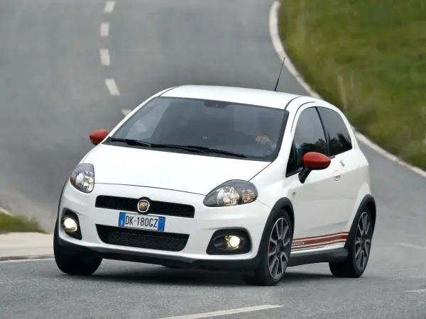 Biały Fiat Punto Abarth z czerwonymi lusterkami i paskami na boku, jadący po krętej drodze.