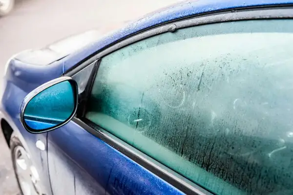 En blå bil med frost på sidorutan. Frågan "hur får man bort imma i bilen" är relevant när det är kallt ute.