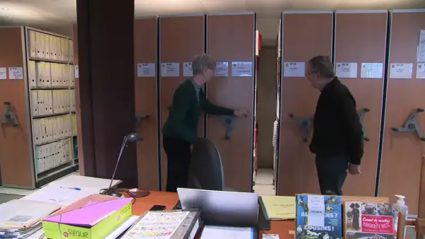 Deux personnes devant des rayonnages d'archives mobiles.