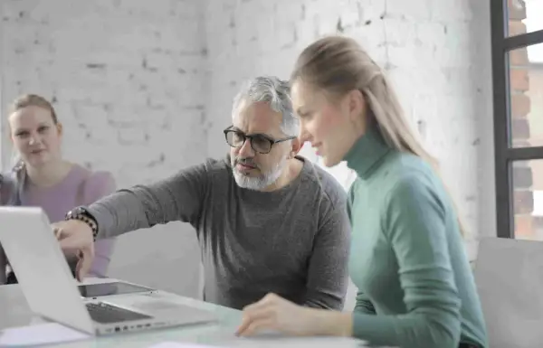 Uomo della generazione boomer spiega qualcosa su un laptop a una collega.