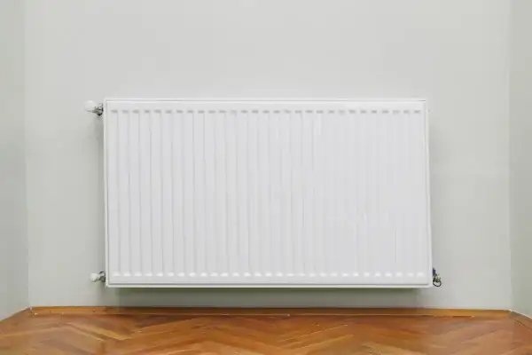 Radiatore bianco moderno su parete chiara, con parquet. Utile per calcolare quanti elementi termosifoni per mq.