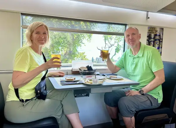 Ett par skålar med öl på ett tåg till München. De njuter av en måltid med bröd, ost och charkuterier medan landskapet susar förbi utanför fönstret.