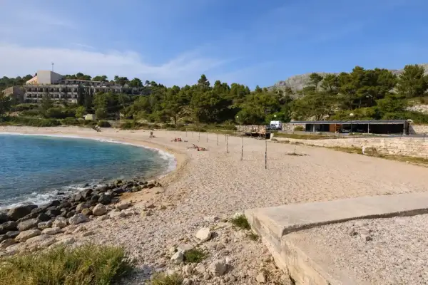 Plaża w Kupari, Chorwacja, z turkusową wodą, kamienistym brzegiem i hotelami w tle.