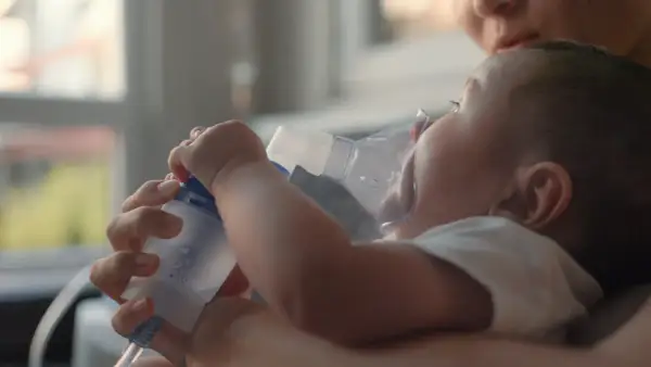 Mama pomaga maluszkowi z mokrym kaszlem u niemowlaka, stosując inhalator.