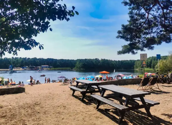 Słoneczny dzień nad jeziorem Średnim Turawa. Ludzie odpoczywają na plaży, kąpią się i pływają.