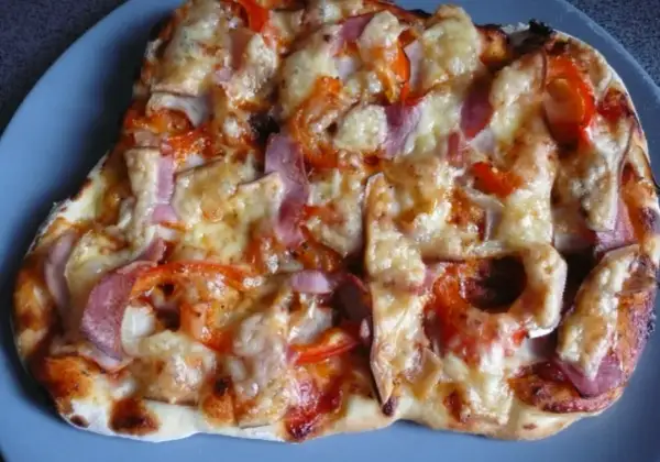Pyszna pizza z szynką, papryką i cebulą, zapieczona pod ciągnącym się serem. Idealna na szybki obiad.