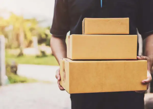 Kurier firmy kurierskiej FedEx niesie trzy paczki.