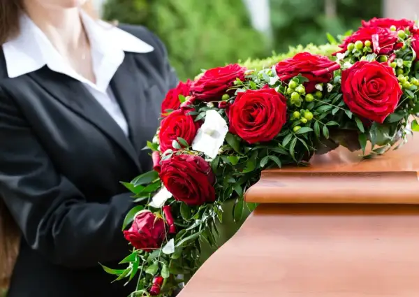 Osoba w czerni kładzie wieniec pogrzebowy z czerwonych róż na trumnie. Wieniec pogrzebowy znaczenie to symbol miłości i pamięci.