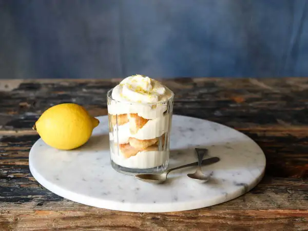 Un délicieux tiramisu aux agrumes, servi dans un verre, avec un citron frais à côté.