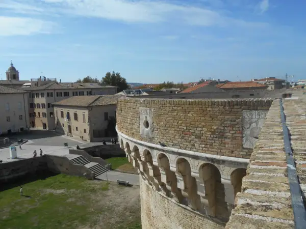 Vista panoramica di Senigallia, Ancona, con un'antica fortezza in primo piano e tetti di tegole rosse sullo sfondo sotto un cielo azzurro.