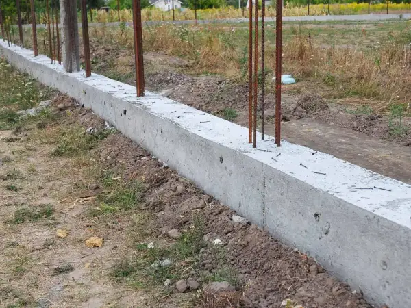 Solidna podmurówka ogrodzenia panelowego z wystającymi prętami zbrojeniowymi, gotowa na montaż.