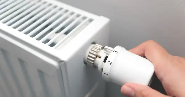 Dłoń kręci termostatem grzejnika, ustawiając temperaturę. Czas zacząć sezon grzewczy.