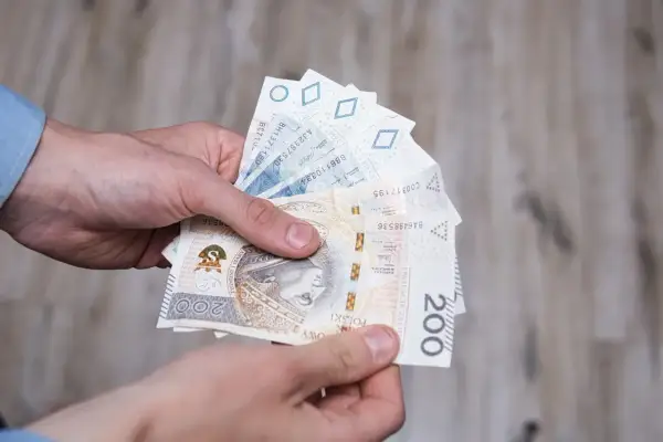 Dłonie trzymają polskie banknoty, w tym 200 zł. Może to symbolizować otrzymanie renty socjalnej z MOPS.