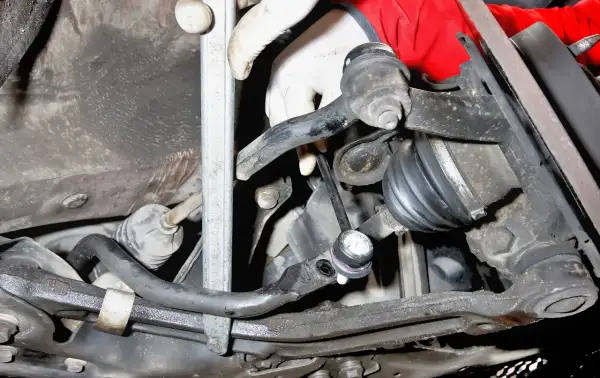 Montaż łącznika stabilizatora Toyota Yaris 1. Widoczna ręka w rękawiczce przykręca element zawieszenia.