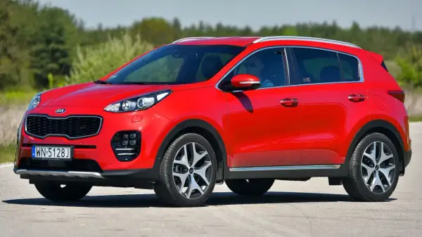 Czerwony Kia Sportage 1. generacji z kierowcą w okularach przeciwsłonecznych jedzie po drodze.