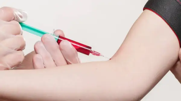 Prélèvement sanguin : une seringue verte et rouge est insérée dans un bras.