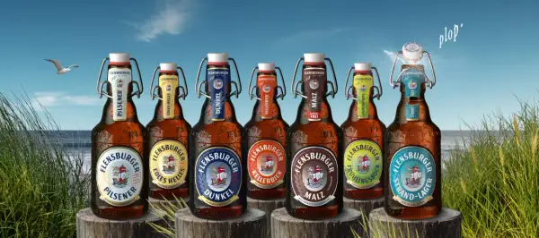 Flensburger Pils Bier Marken am Strand. Eine Möwe fliegt über das Meer, während die Flaschen mit Bügelverschluss im Gras stehen.
