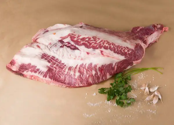 Un corte de carne cruda, con grasa marmoleada, listo para convertirse en un delicioso pastrami que es. Acompañado de perejil y ajos.