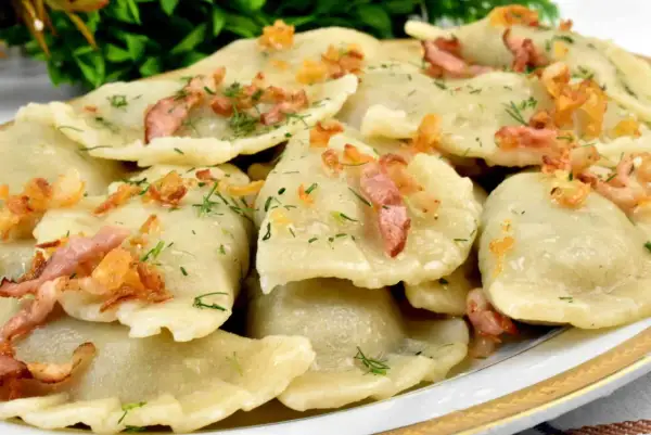 Talerz pełen pysznych, domowych pierogów z młodej kapusty, posypanych skwarkami i koperkiem.