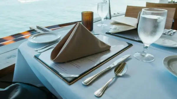 Stół w restauracji z widokiem na morze, nakryty do posiłku, z menu i kieliszkiem wody.